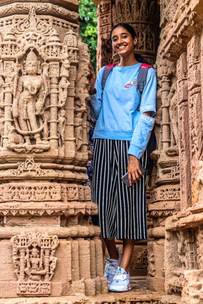 A woman stands smiling amidst intricately carved stone pillars of an ancient temple, showcasing exquisite traditional architecture.