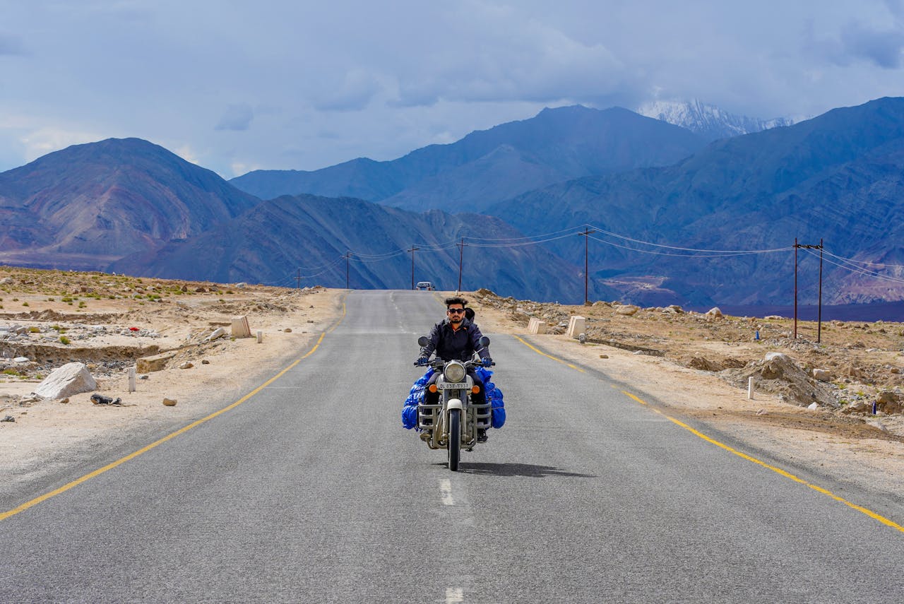 A solitary biker traveling through the rugged terrain of Leh, surrounded by majestic mountains.